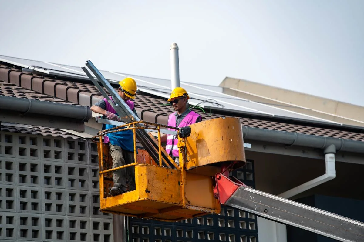 Two Emit Solar installers on a boom lift bringing a panel rail up to the roof