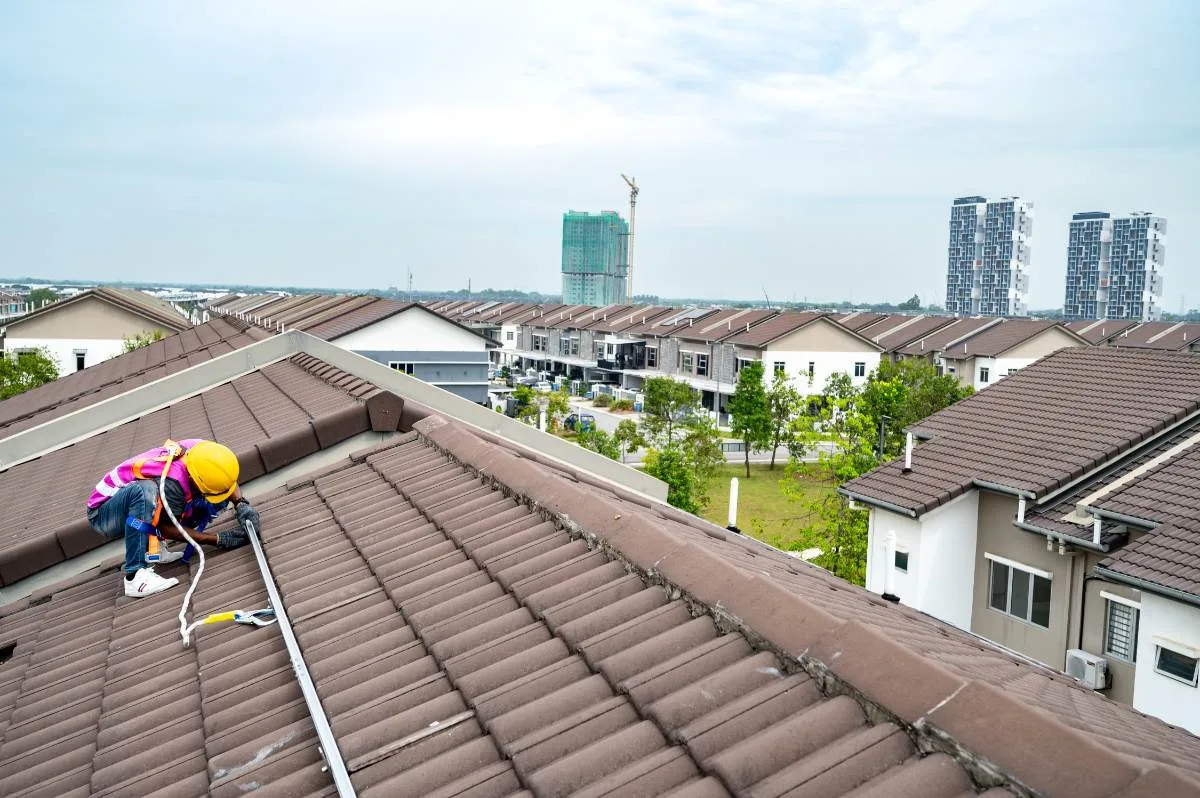 Emit Solar installer fixing a rail on a terrace-house roof, with the housing estate behind