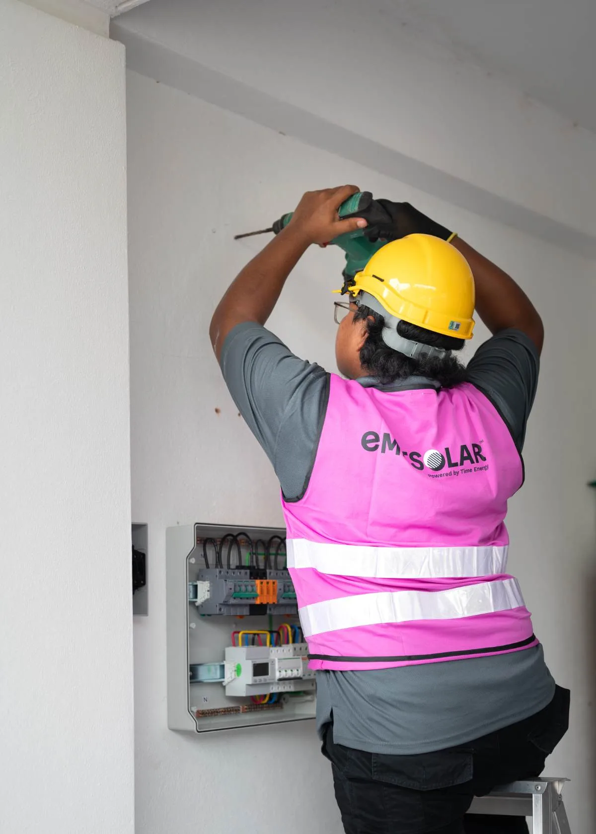 Emit Solar installer in a pink vest and hard hat wiring the distribution board