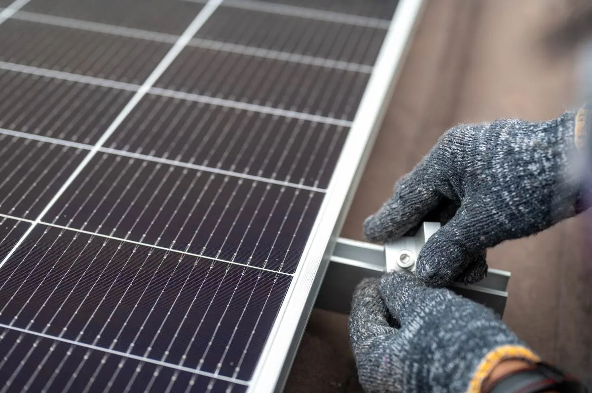 Gloved hands fixing a clamp to a solar panel rail