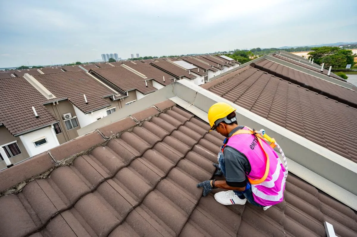 Emit Solar installer kneeling on a terrace-house roof above a housing estate